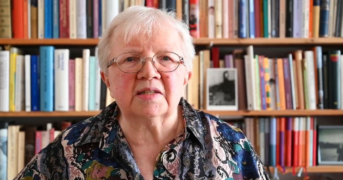 Portraitaufnahme Luise F. Pusch, eine weißhaarige 75-Jährige, vor ihrem Regal voller Bücher
