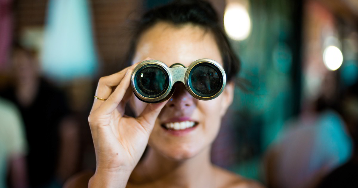 Frau schaut durch Fernglas - Genau hinschauen um Vorurteile im Journalismus aufzulösen