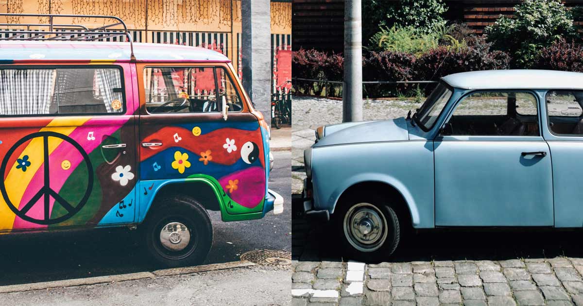 Ein buntbemalter VW-Bulli und ein hellblauer Trabant stehen sich Schnauze an Schnauze gegenüber