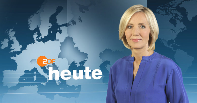 Petra Gerster steht mit blauer Bluse vor dem Nachrichtenhintergrund der heute-Sendung