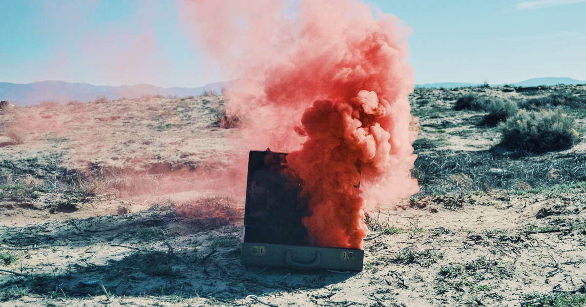 In einer Wüstenlandschaft steht ein Koffer aus dem roter Qualm hochsteigt
