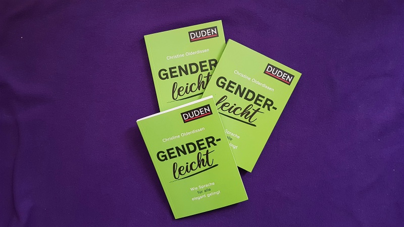 Drei Exemplare des Buchs Genderleicht liegen auf einem lilafarbenen Untergrund