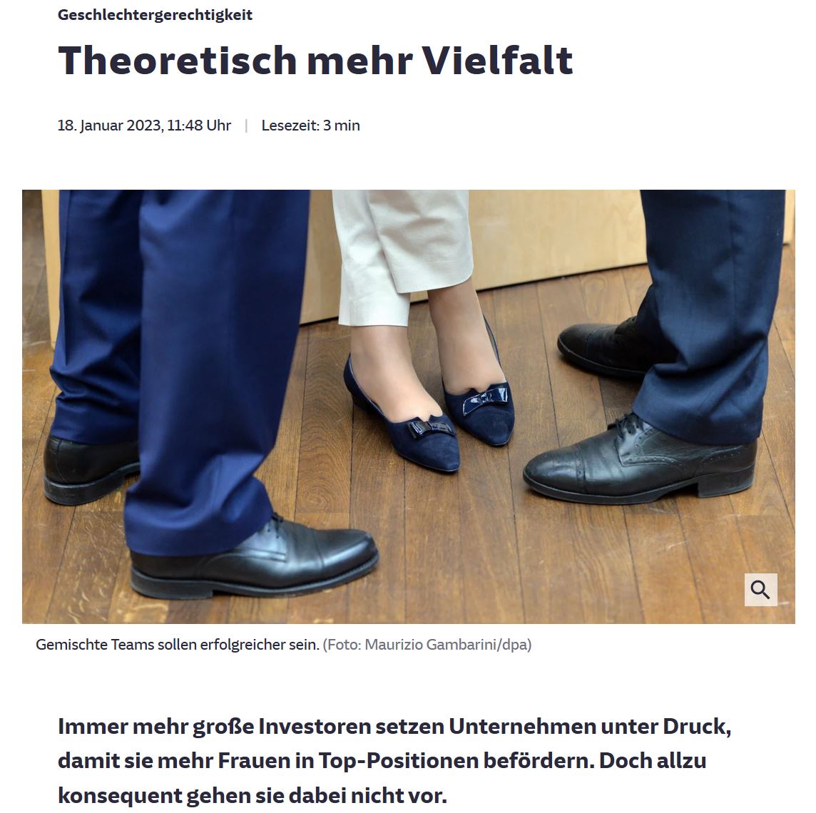Zwischen zwei Beinen mit Anzughosen sind die Beine einer Frau mit einer weißen Hose und blauen flachen Damenschuhe zu sehen