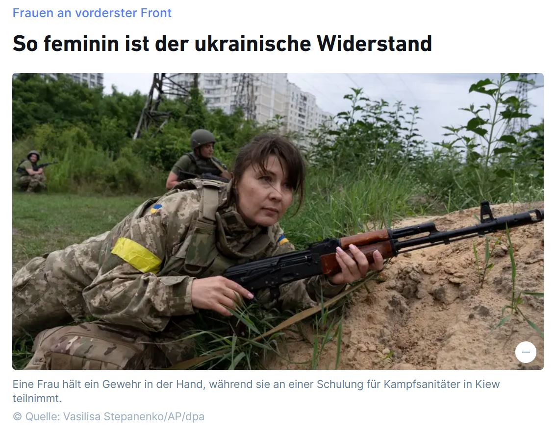 Frau in Kampfuniform liegt mit Gewehr in der Hand auf dem Boden. Hinter ihr sind zwei weitere Soldaten zu sehen.