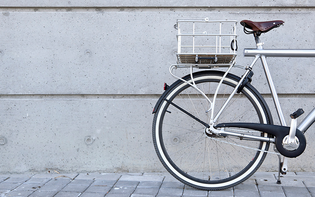 Silberfarbenes Fahrrad steht parallel vor einer grauen Mauer