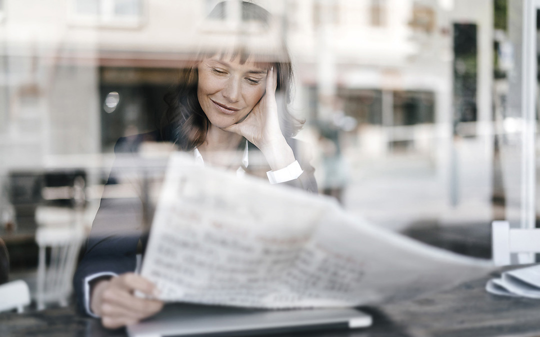 Frau liest Zeitung, fotografiert hinter der Glasscheibe eines Cafés