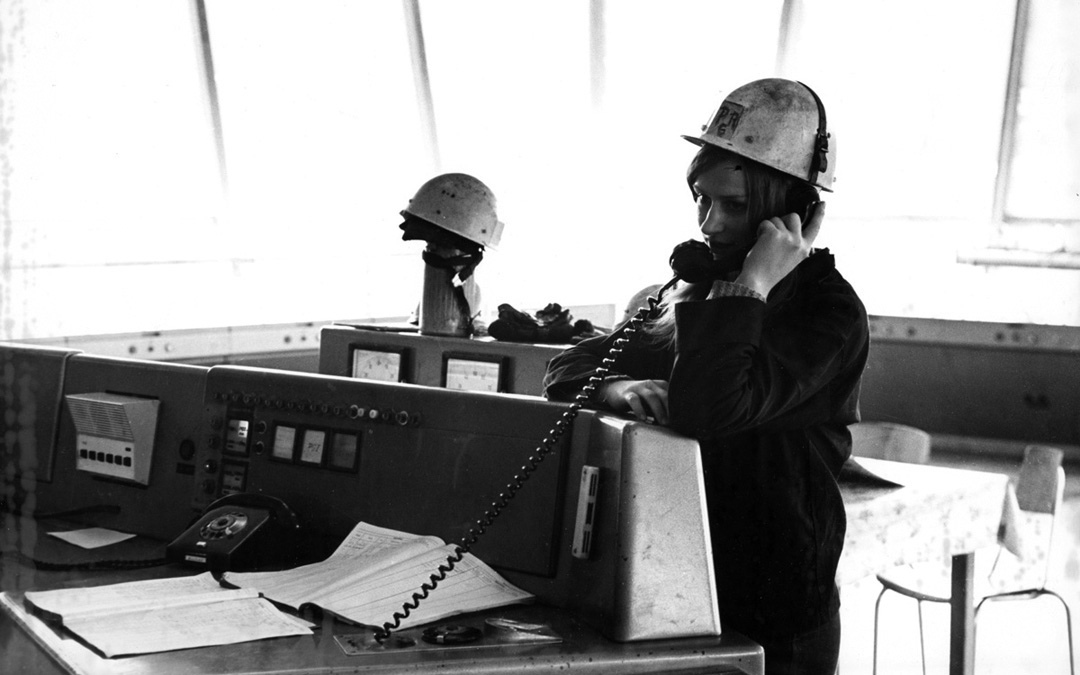 Schwarz-weiß-Foto: Frau mit Helm in der Schaltzentrale eines DDR-Industriebetriebs