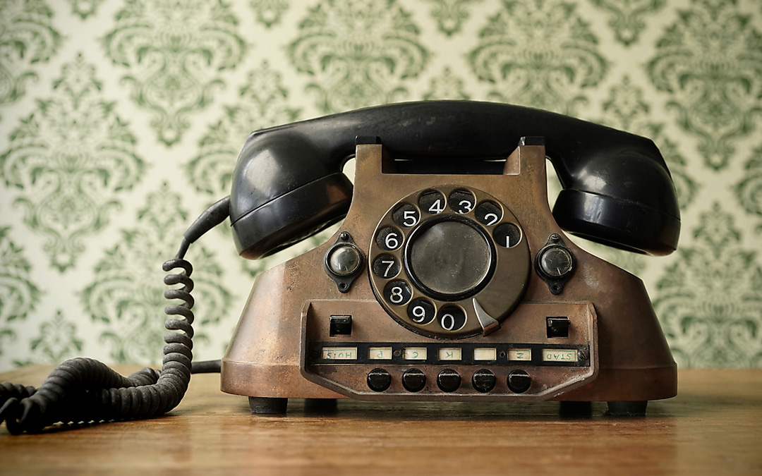 Altes Telefon mit Hörer und geringeltem Kabel vor einer grüngemusterten Tapete