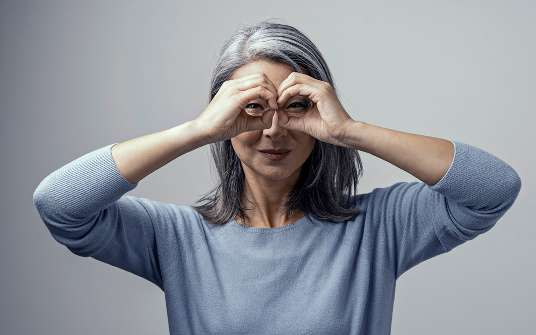 Grauhaarige Frau schaut durch ihre Finger