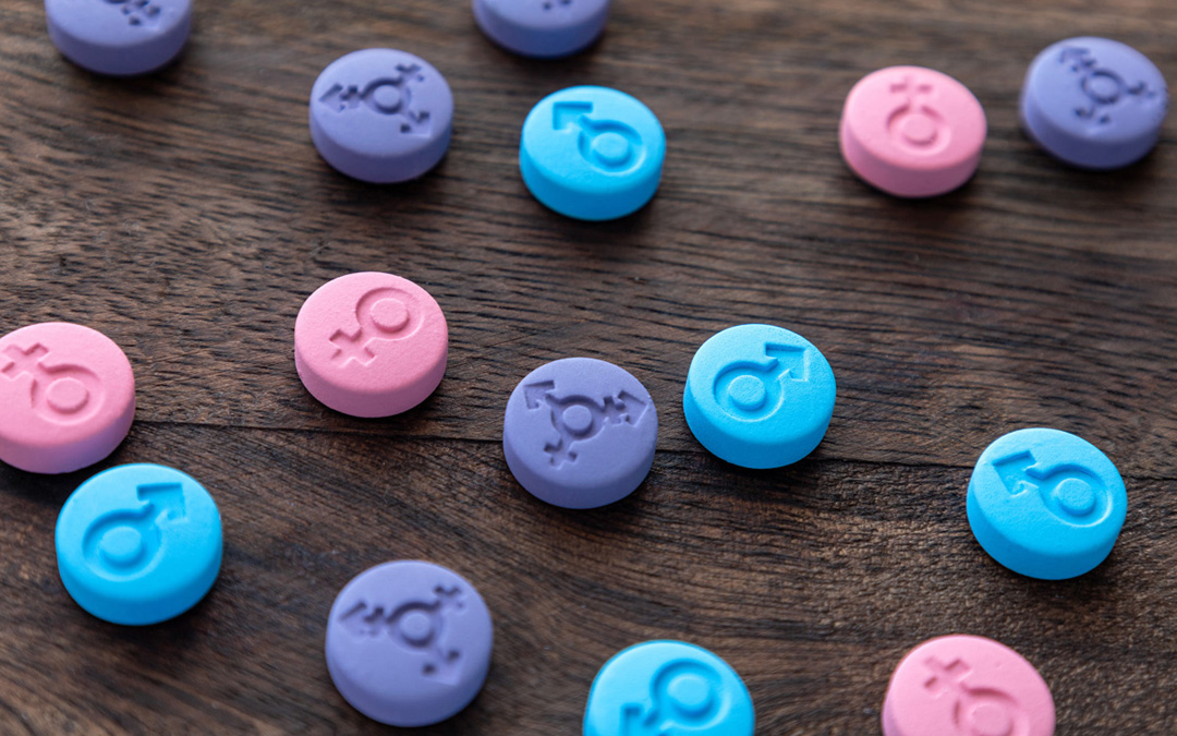 Hellblaue, rosa- und lilafarbene Pillen mit eingefrästen Genderzeichen: maskulin, feminin und divers