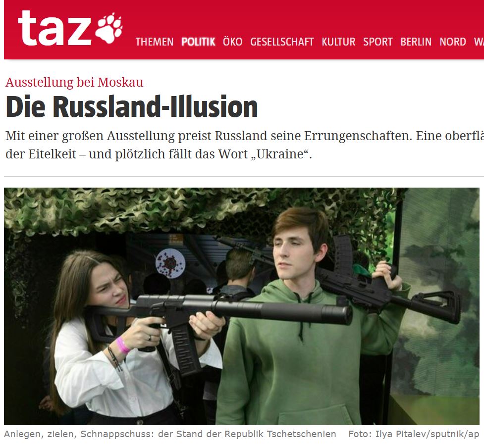 Screenshot junge Frau hält testweise ein großes Maschinengewehr im Anschlag. Ein junger Mann neben ihr hat ein ähnliches Gewehr geschultert und schaut ihr zu.