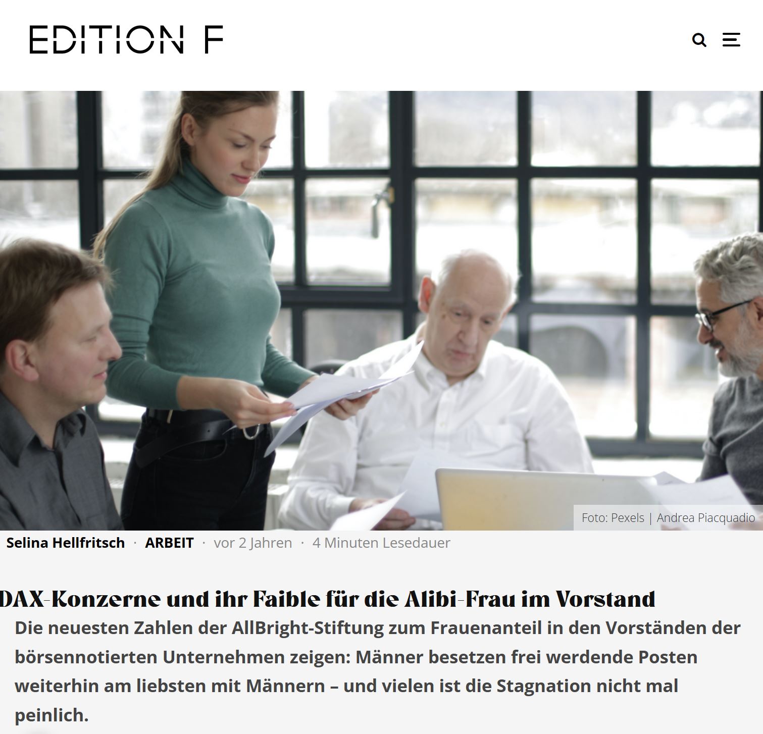 Junge Frau steht neben älteren, sitzenden Männern bei einer Bürobesprechung