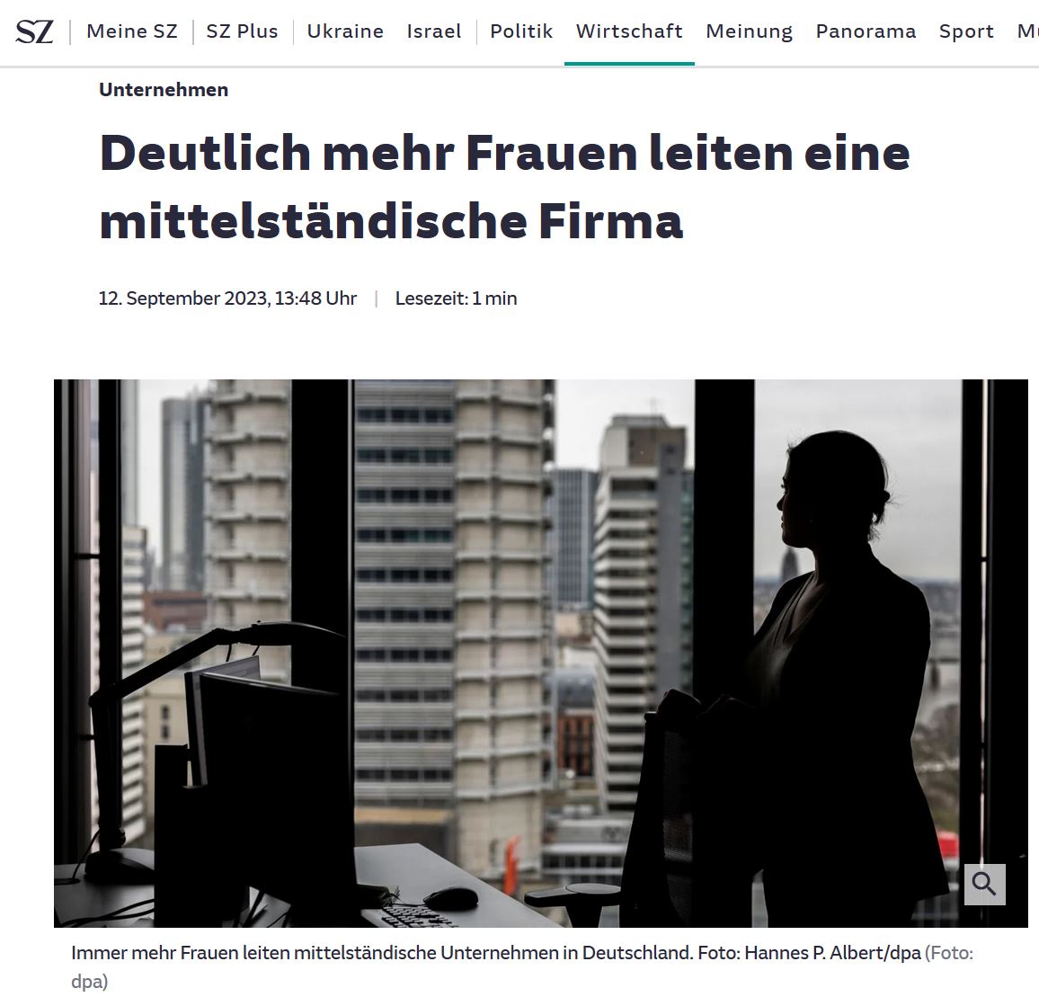 Frau steht im Gegenlicht eines Büros und schaut auf die Skyline mit Hochhäusern