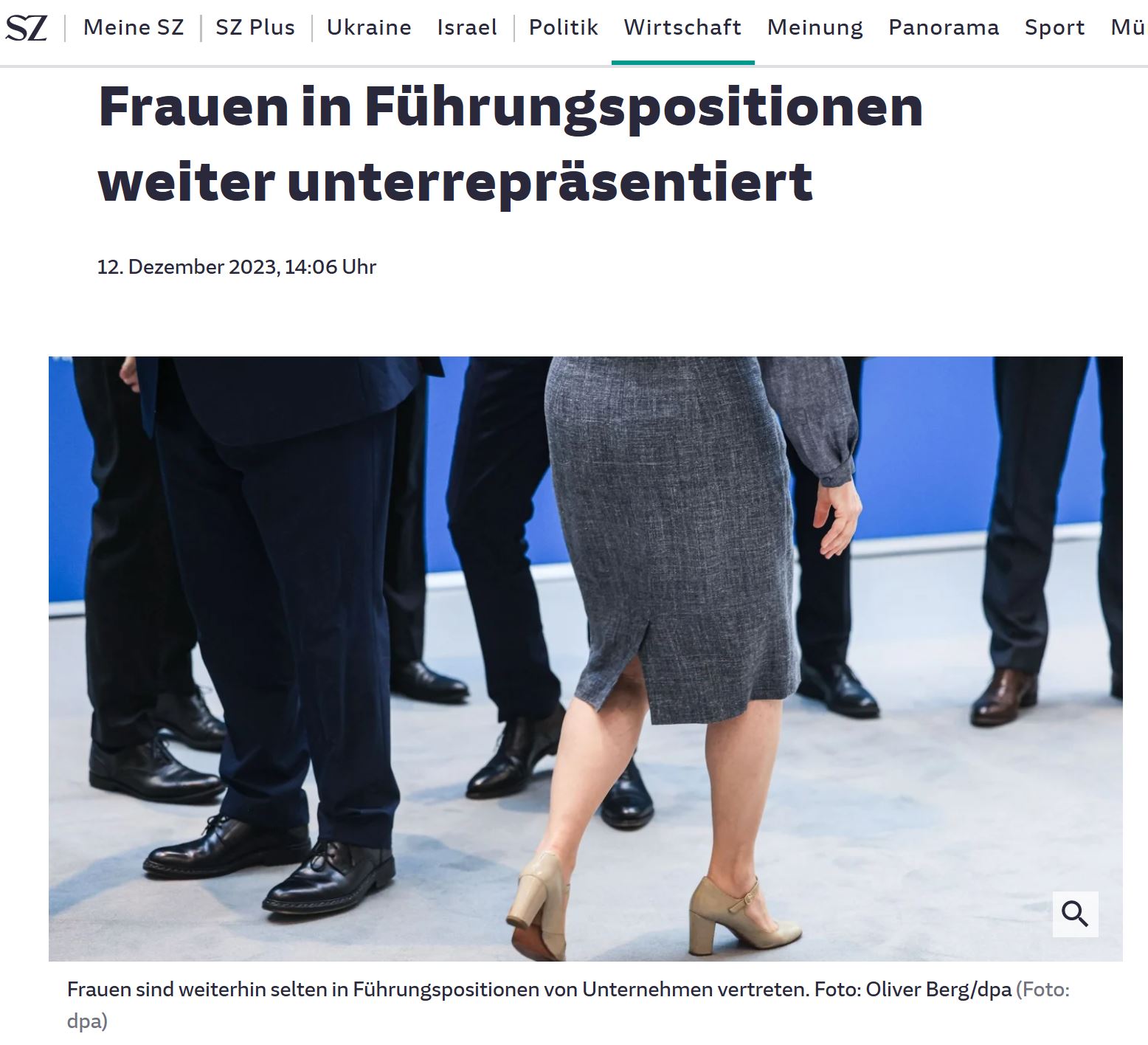 Frau im grauen, engsitzenden Kleid läuft an sechs Männern vorbei. Alle sind nur ab Bauch abwärts fotografiert.
