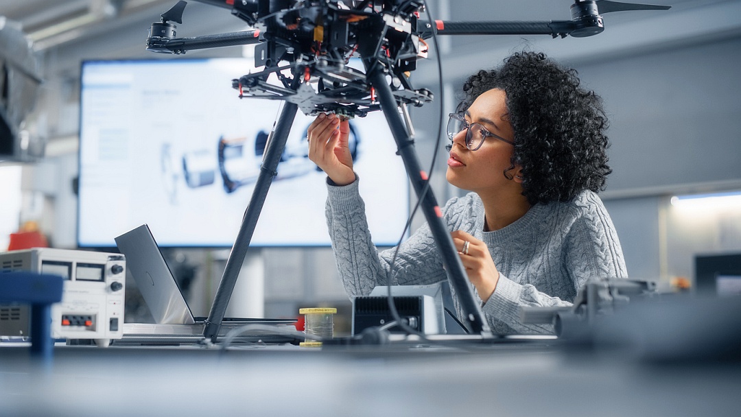 Stockfoto Ingenieurin junge schwarze Frau mit Brille stell in einem Forschungslabor an einem technischen Gerät etwas ein.