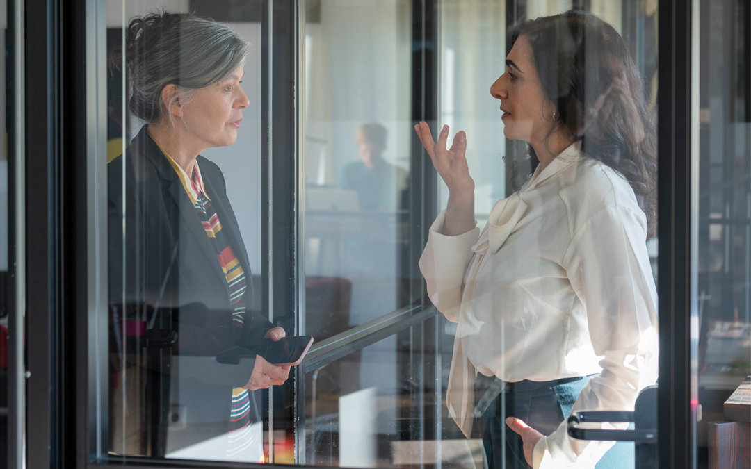 Führungsfrauen im Gespräch ©Anita Back Dunkelhaarige Frau stützt sich auf einen Tisch in herausfordernder Pose