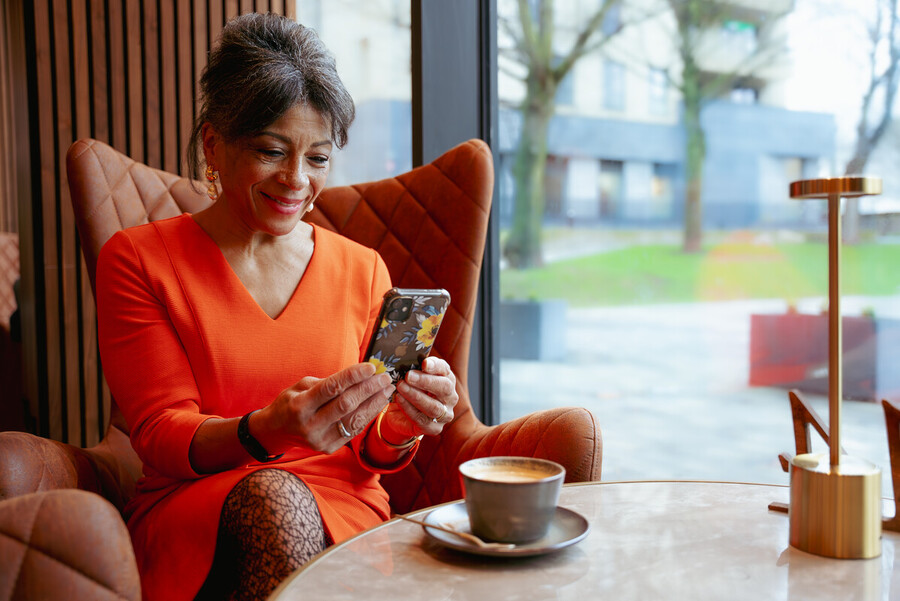 In einem Café sitzt eine elegant gekleidete Seniorein und schaut in ihr Smartphone