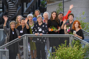 Auf einer Dachterasse stehen viele junge und ältere Frauen und jubeln in die Kamera