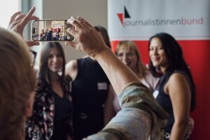 Frau fotografiert mit Smartphone Gruppe von vier jungen Frauen vor RollUp Journalistinnenbund