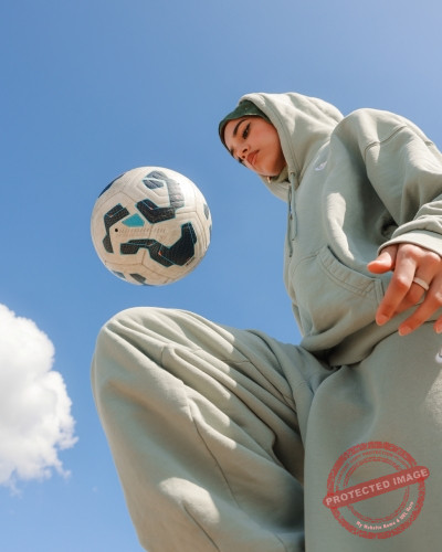 Junge Frau im grauen Trainingsanzug balanciert einen Fu&szlig;ball