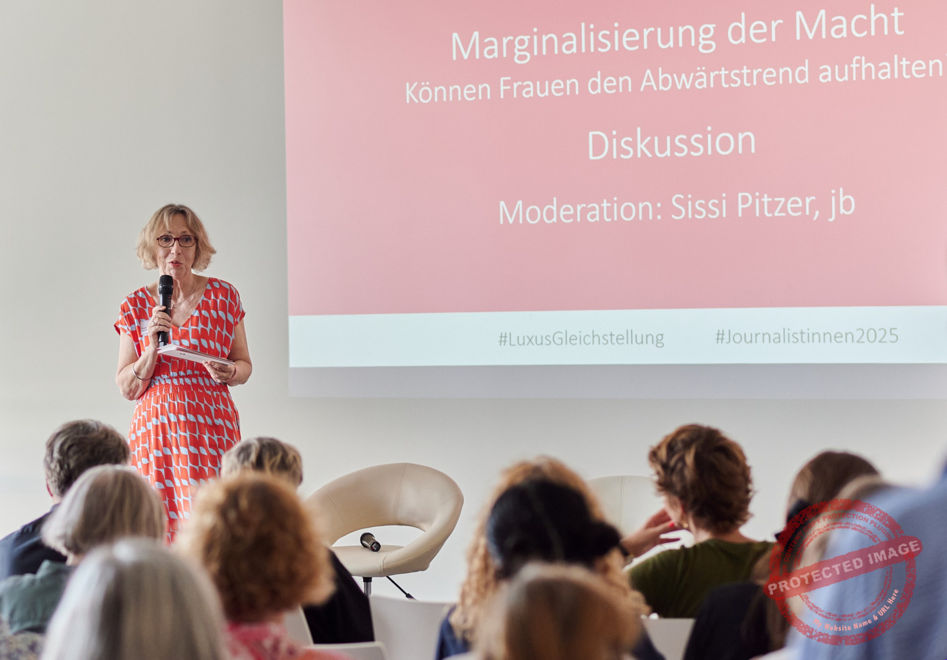 Eine Frau steht bei einer Moderation auf der B&uuml;hne vor Publikum
